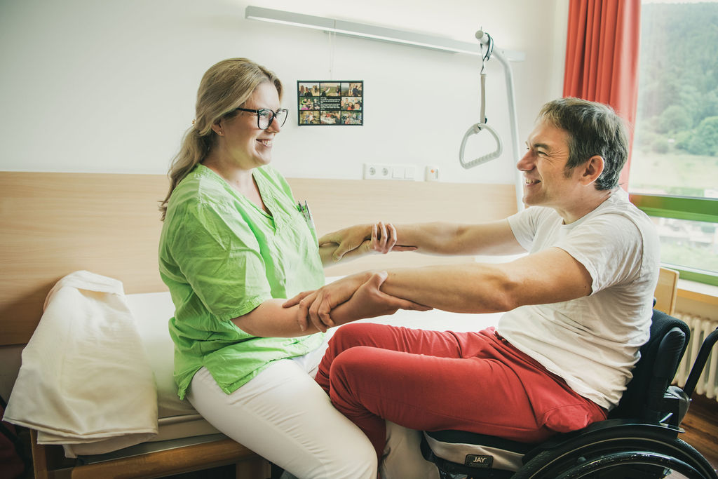 Eine Pflegerin hilft einem Patienten aus dem Rollstuhl ins Bett