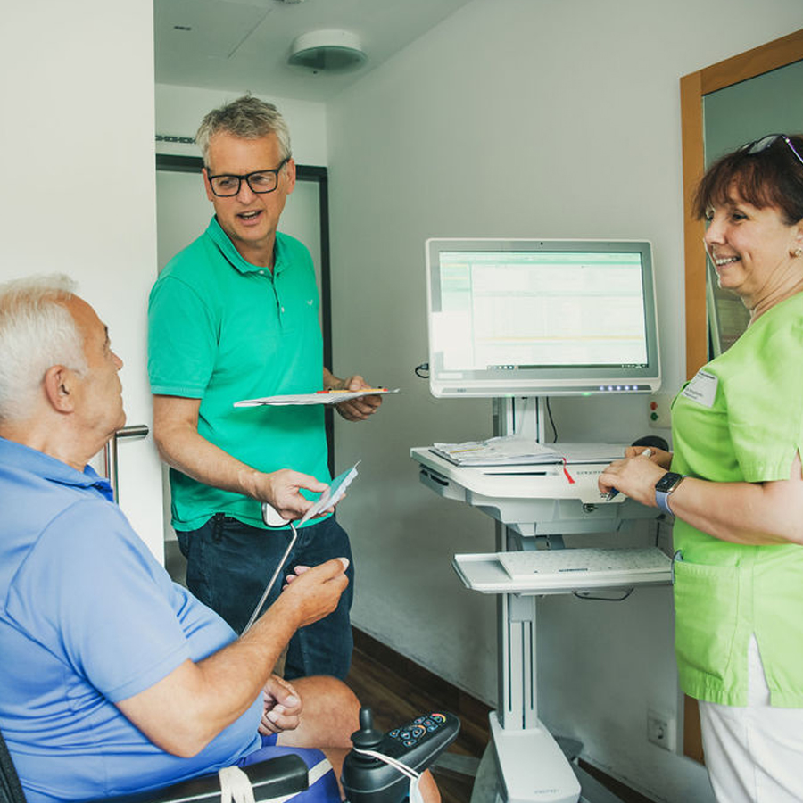 Patient im Behandlungszimmer mit Arzt und Pflegekraft